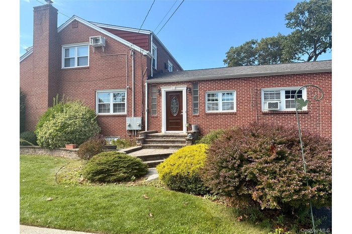 View of front facade featuring brick siding, a chimney, a front yard, and a wall unit AC