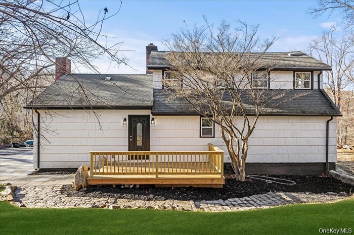 Back of house featuring a deck, a shingled roof, a yard, and a chimney