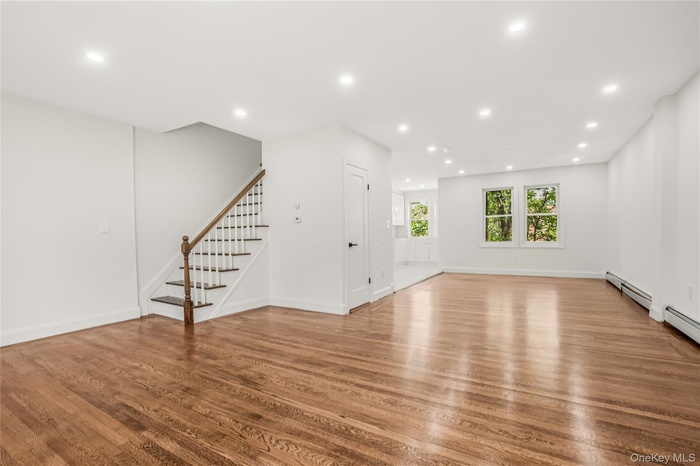Unfurnished living room featuring stairs, recessed lighting, light wood-type flooring, and a baseboard heating unit