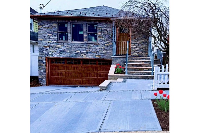 View of front of property featuring a garage, stone siding, and driveway