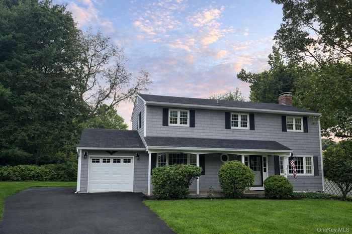 Traditional home with driveway, a garage, a chimney, a lawn, and a shingled roof