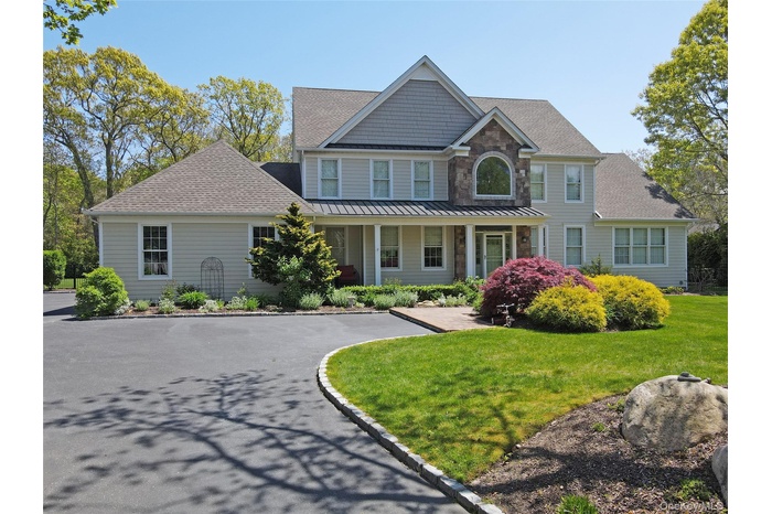 View of front of house with roof with shingles, a front yard, covered porch, and stone siding