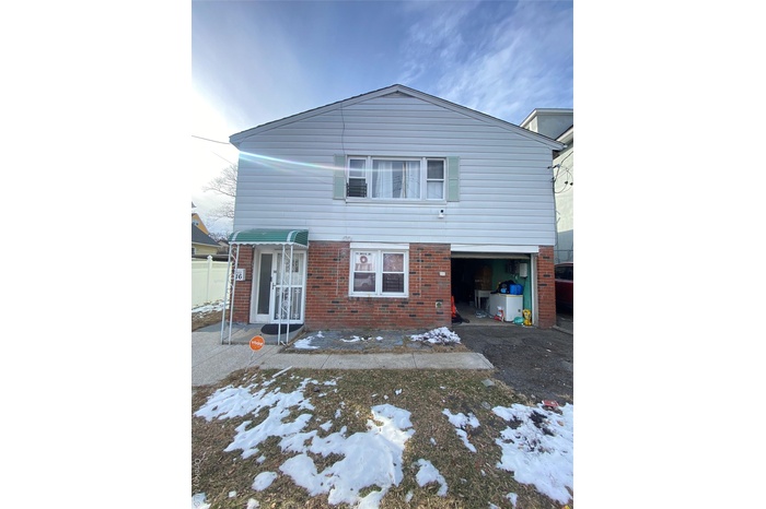 Snow covered rear of property with brick siding, a patio, and an attached garage