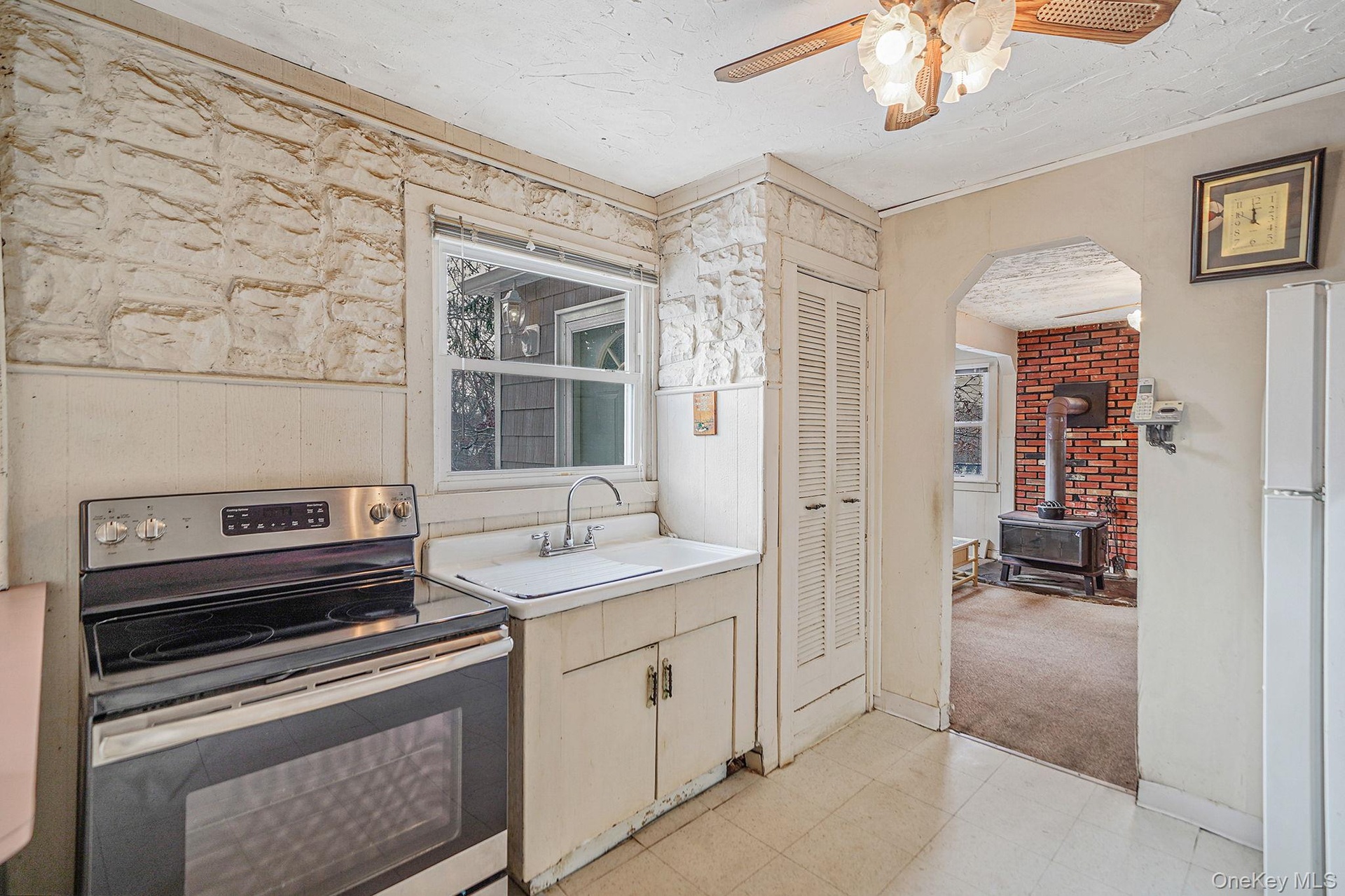 Kitchen featuring stainless steel range with electric cooktop, light countertops, freestanding refrigerator, a wood stove, and a ceiling fan