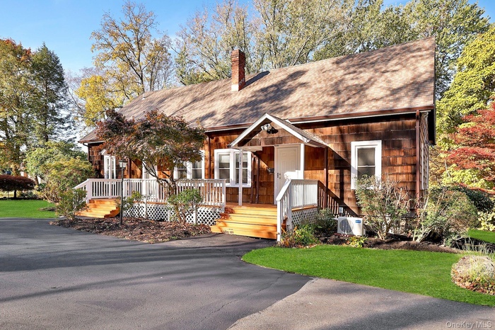 View of front of house with a shingled roof, a deck, a chimney, and a front yard