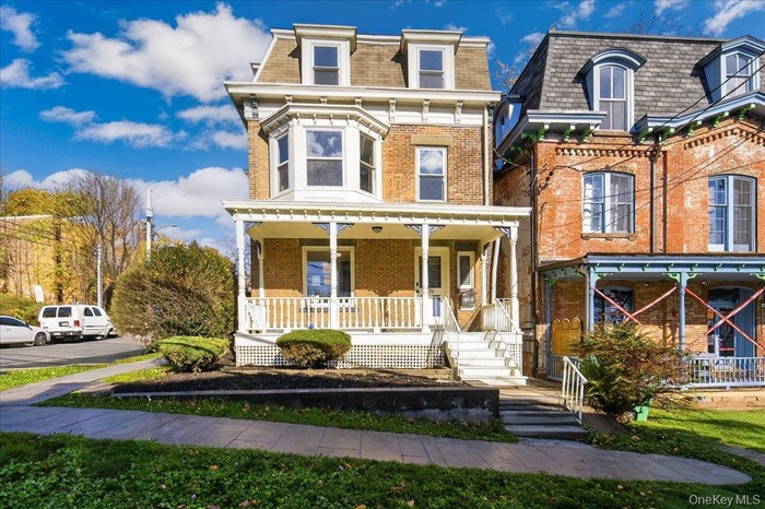 Victorian style home with a porch, mansard roof, and brick siding