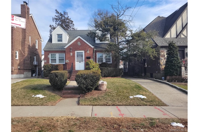 View of front of house featuring brick siding, a front yard, and roof with shingles