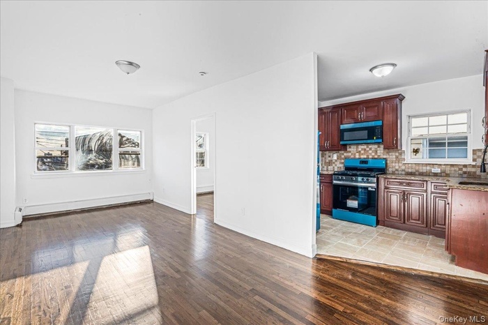 Kitchen featuring light wood-style flooring, appliances with stainless steel finishes, light stone countertops, backsplash, and a baseboard radiator