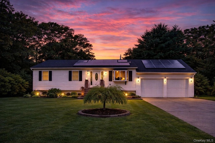 Ranch-style home featuring driveway, a front lawn, solar panels, and an attached garage