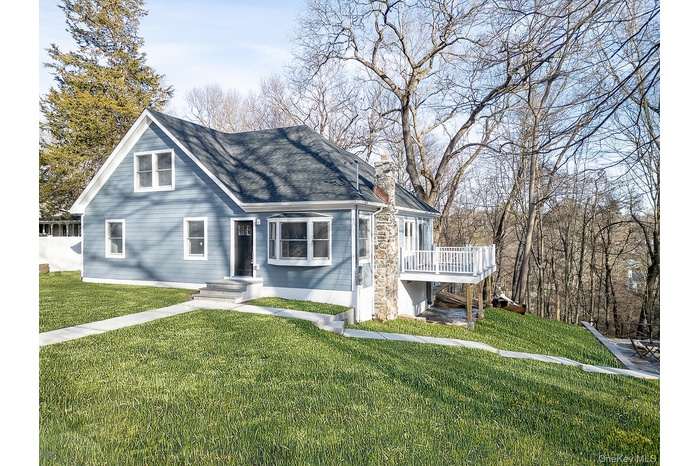 View of front facade with a front lawn, stone siding, and a shingled roof