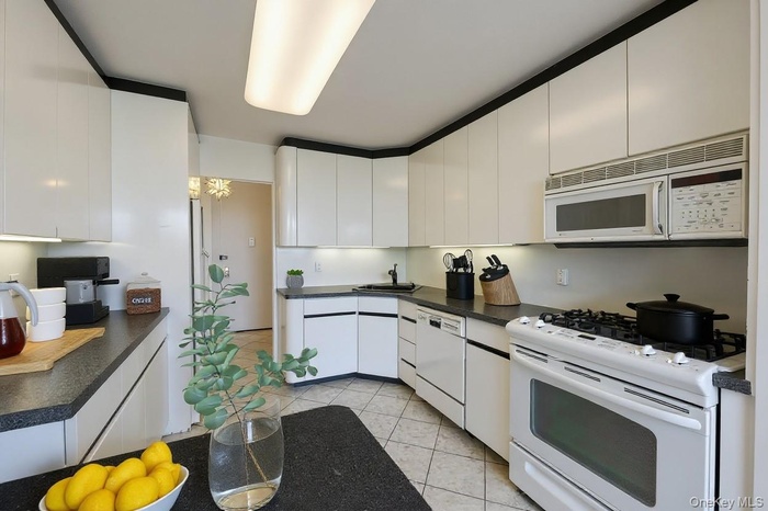 Kitchen featuring white appliances, white cabinetry, dark countertops, light tile patterned floors, and modern cabinets