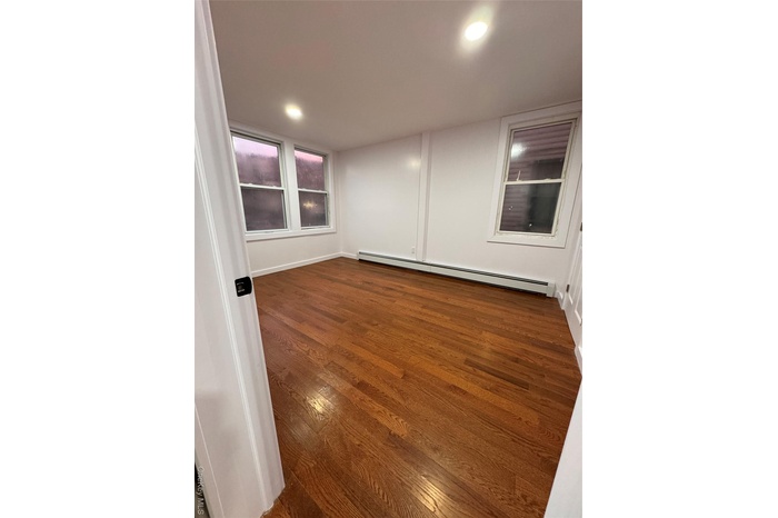 Unfurnished room with dark wood-style flooring, a baseboard heating unit, and recessed lighting