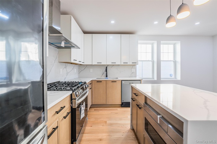 Kitchen with stainless steel appliances, wall chimney range hood, hanging light fixtures, light stone counters, and recessed lighting