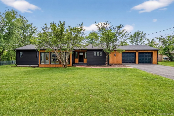 View of front facade with a front yard, an attached garage, and a shingled roof