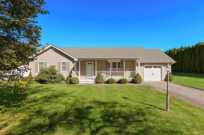 Single story home with covered porch, a front lawn, an attached garage, driveway, and a shingled roof