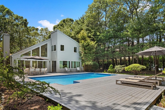 Outdoor pool with a patio area, view of wooded area, and a deck