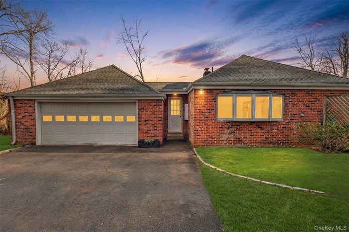 Ranch-style home with a front yard, brick siding, a shingled roof, and driveway