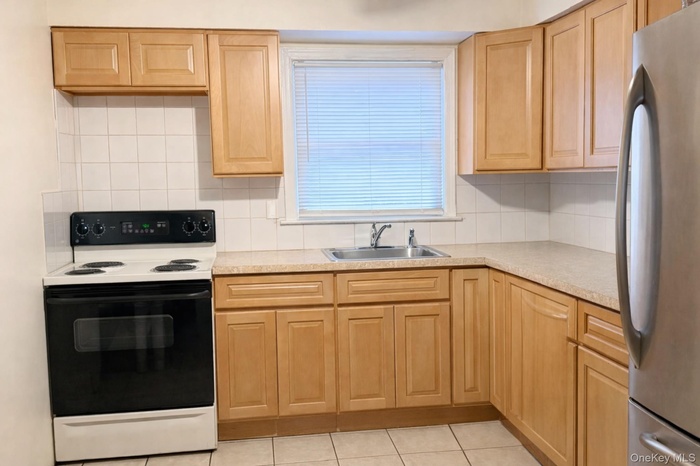 Kitchen with electric range oven, freestanding refrigerator, light brown cabinets, and light countertops