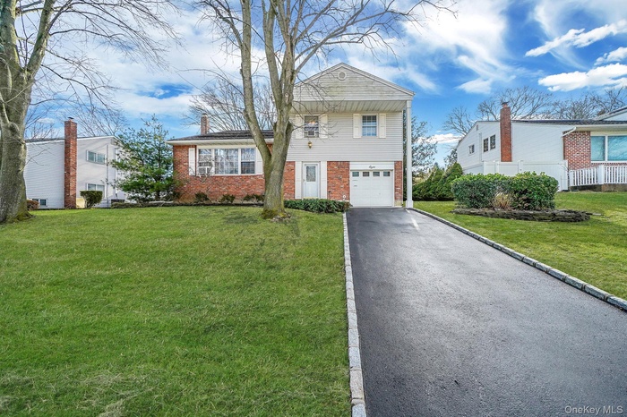 View of front of home with a front yard, brick siding, asphalt driveway, and an attached garage