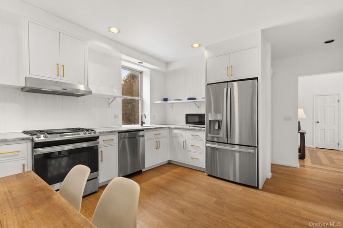 Kitchen with open shelves, white cabinets, stainless steel appliances, light wood finished floors, and under cabinet range hood