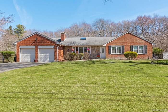 Ranch-style home featuring driveway, a front yard, a garage, brick siding, and a chimney