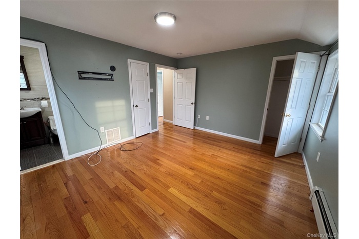 Unfurnished bedroom with a baseboard radiator, ensuite bath, and light wood-style floors