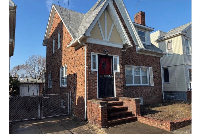 Tudor home with a gate, brick siding, roof with shingles, and a chimney