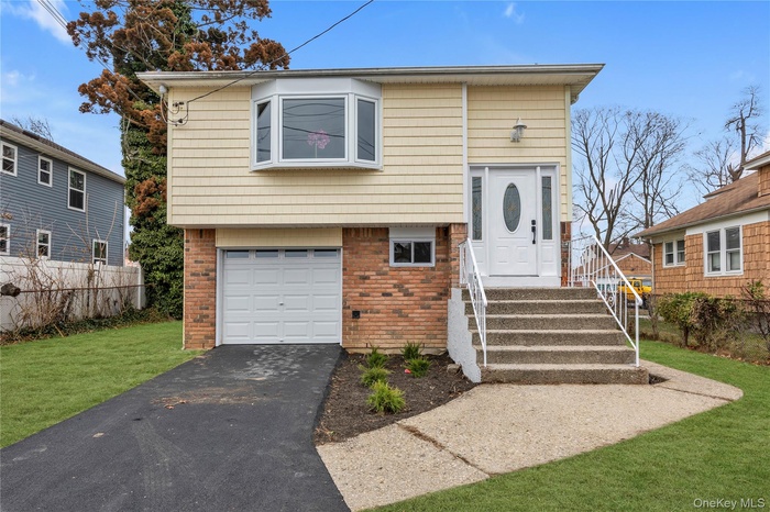 Split foyer home with brick siding, an attached garage, a front lawn, and asphalt driveway