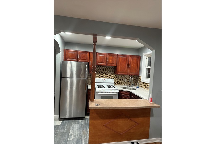 Kitchen with stainless steel range oven, fridge, light countertops, arched walkways, and decorative backsplash