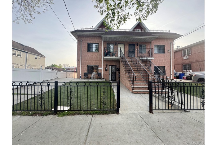 Multi unit property featuring a porch, brick siding, a fenced front yard, stairway, and a front lawn