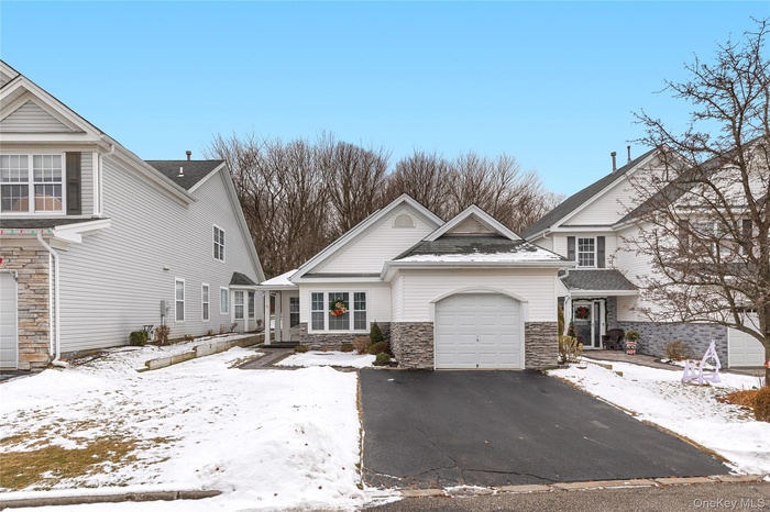Traditional home featuring stone siding, an attached garage, and driveway