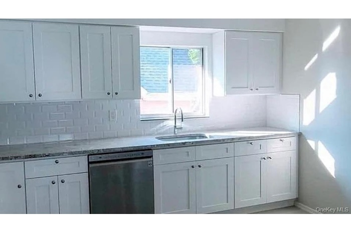 Kitchen with stainless steel dishwasher, white cabinetry, light stone counters, and decorative backsplash