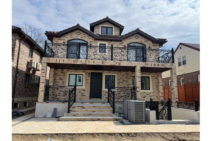 View of front facade featuring a porch, brick siding, central AC unit, and a balcony