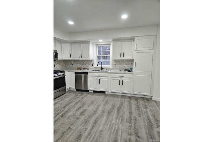 Kitchen with stainless steel appliances, white cabinets, light countertops, light wood finished floors, and recessed lighting
