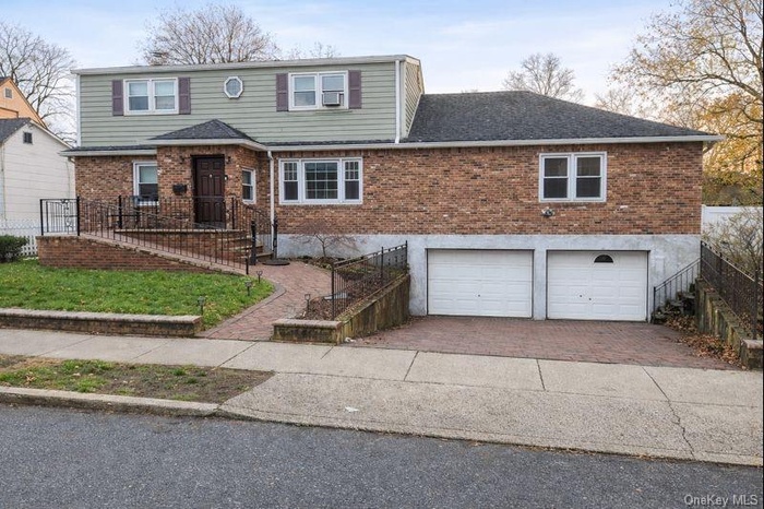 View of front of property with brick siding, decorative driveway, an attached garage, and stairs