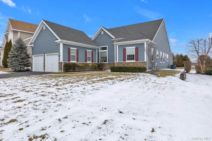 View of front facade featuring a garage, stone siding, a shingled roof, and driveway
