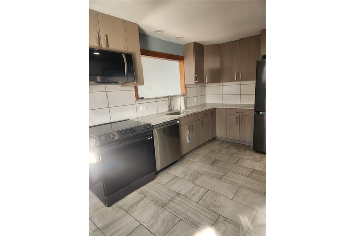 Kitchen with range, dishwasher, fridge, light stone counters, and backsplash