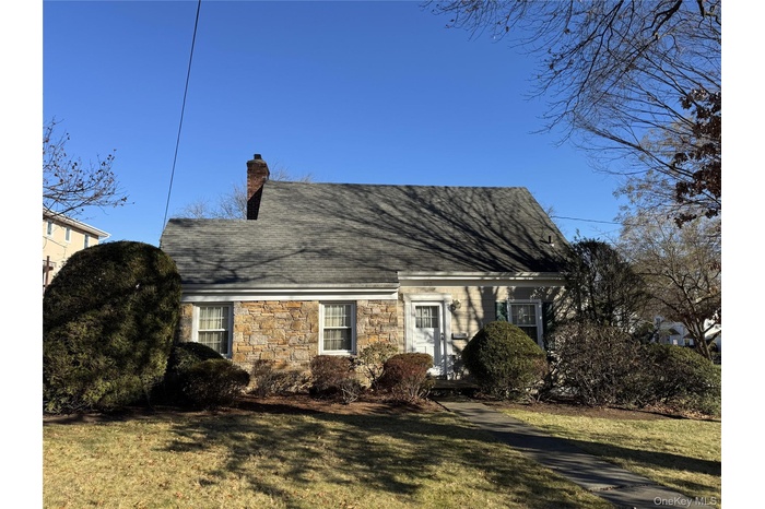 Cape cod house with stone siding, a chimney, and a front lawn