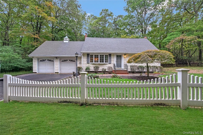 View of front facade with a chimney, a fenced front yard, covered porch, and driveway