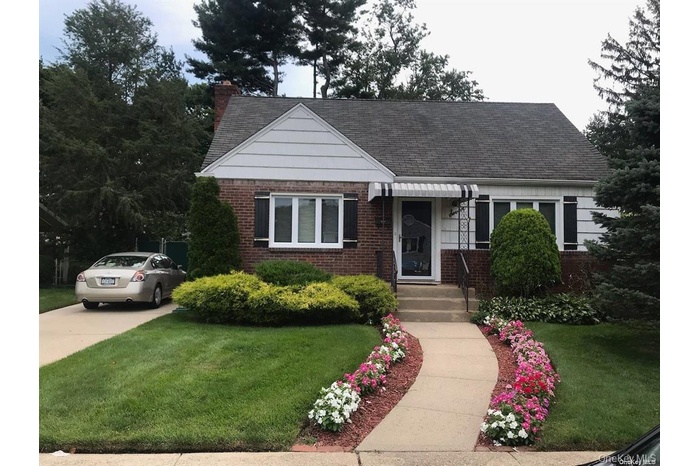 View of front of house featuring brick siding, a front yard, a chimney, and roof with shingles