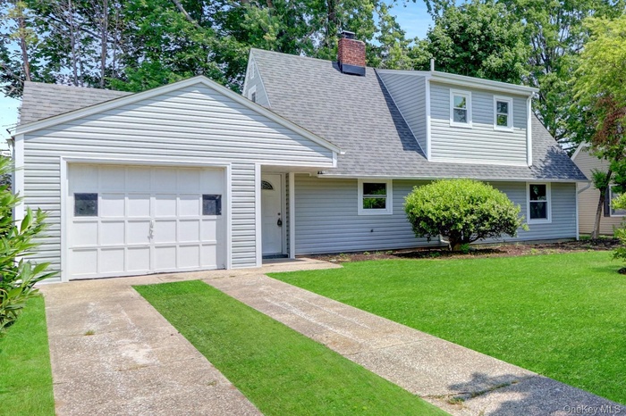 View of front of home with a shingled roof, a front lawn, a chimney, a garage, and driveway