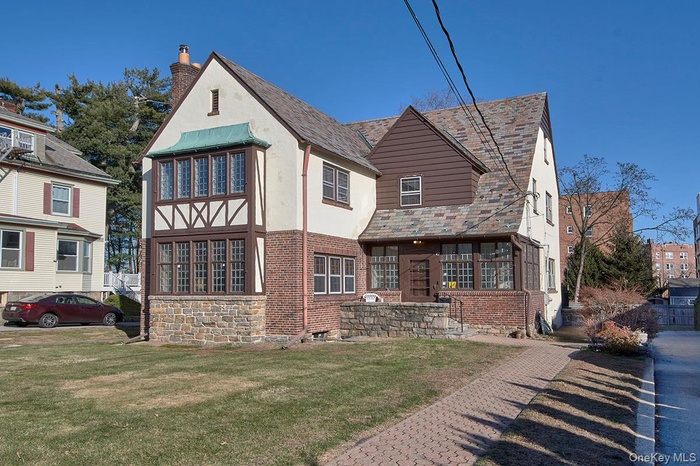 View of front facade featuring brick siding, a chimney, a front lawn, and stucco siding