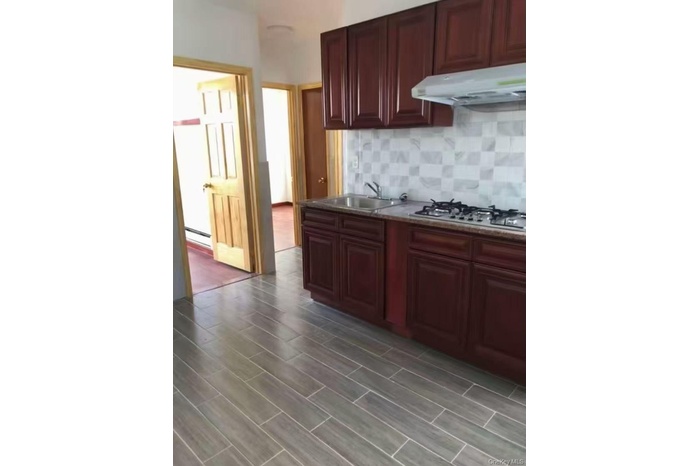 Kitchen with reddish brown cabinets, under cabinet range hood, tasteful backsplash, wood finish floors, and gas cooktop