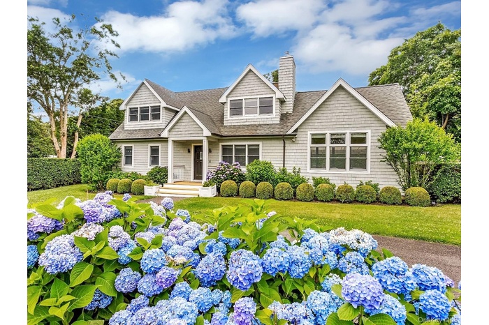 View of front of house with a shingled roof, a chimney, and a front yard
