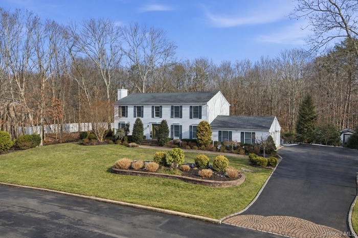 Colonial house featuring a front yard, asphalt driveway, and a chimney