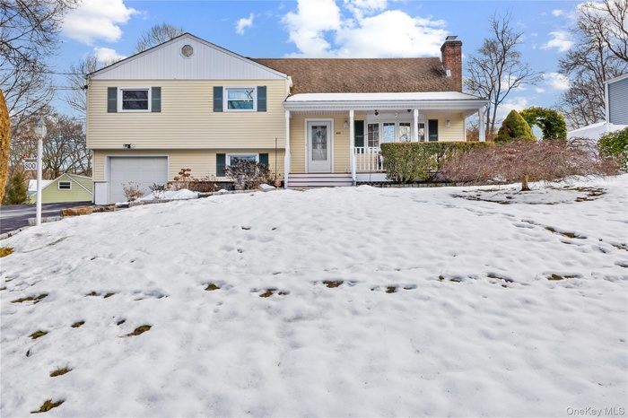 Tri-level home featuring covered porch, a garage, and a chimney