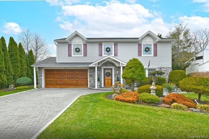 View of front facade with stone siding, decorative driveway, an attached garage, and a front yard