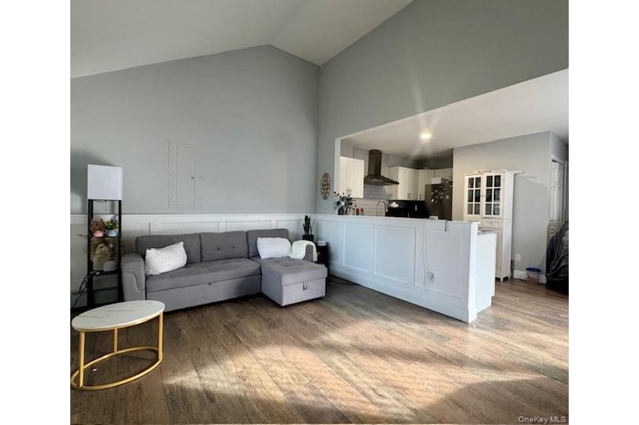 Living area featuring light wood-style floors, electric panel, a wainscoted wall, and high vaulted ceiling