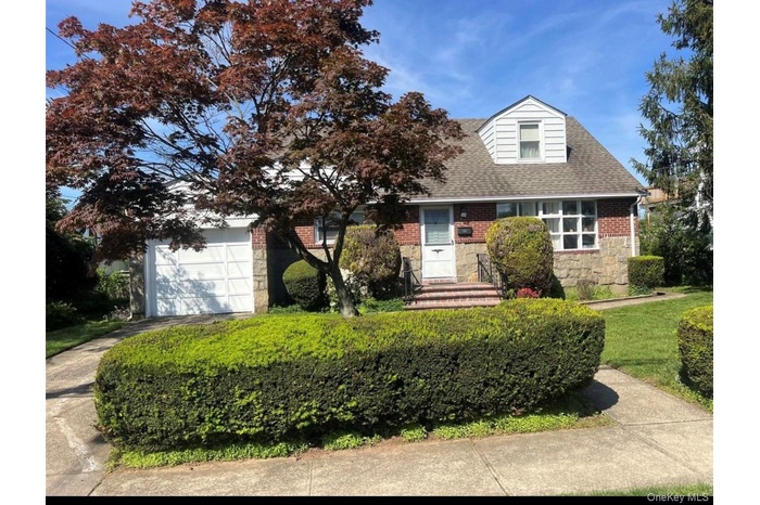 View of front of home with stone siding, a shingled roof, driveway, a front lawn, and brick siding