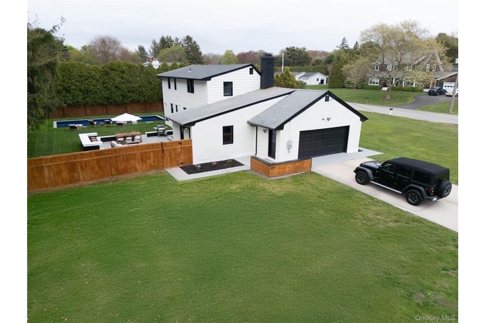 Back of house with concrete driveway, a chimney, an attached garage, brick siding, and view of wooded area
